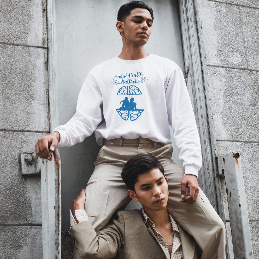 Two individuals standing against a textured wall, one wearing a white sweatshirt with text and graphics.